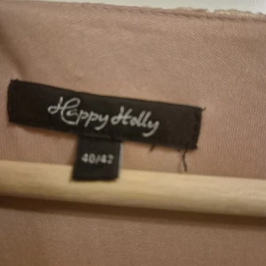 Ljusrosa spetsklänning från Happy Holly - Superfin ljusrosa långklänning från Happy Holly med vacker spets upptill och plisserad kjol. Klänningen har romantiska spetsdetaljer med blommönster och en flowy känsla. Perfekt för dig som vill sticka ut med en elegant och feminin look.