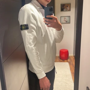 Vit half zip sweatshirt Stone Island - Vit långärmad sweatshirt från Stone Island med klassisk patch på vänster ärm. Tröjan har half zip-dragkedja och hög krage. Tillverkad i mjuk bomull, perfekt för en clean och stilren look.
