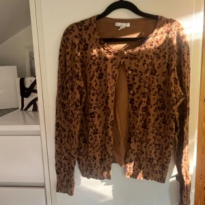 kofta från H&M - Säljer en brun leopardmönstrad kofta från H&M Basics i storlek S. Koftan har rund halsringning, knappar framtill och ribbade muddar vid ärmsluten. Perfekt för dig som vill sticka ut med ett djurmönster i garderoben.