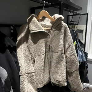 Beige teddyjacka från H&M - Mysig beige teddyjacka från H&M med dragkedja framtill. Jackan har långa ärmar och en hög krage för extra värme. Perfekt för kyliga dagar och ger en trendig look. 🧥✨
