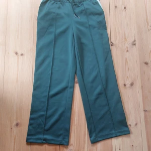 Gröna träningsbyxor från H&M Move - Snygga gröna träningsbyxor från HM Move med vita ränder längs sidorna. Byxorna har en loose passform och dragsko i midjan för justerbar passform.  M men passar L (mig) bra 