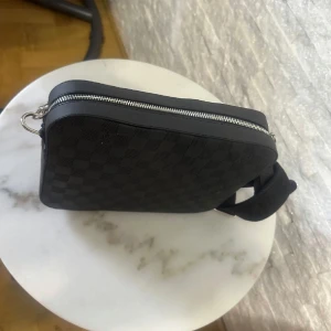 Svart rutig axelväska med dragkedja - Snygg svart axelväska med ett klassiskt rutigt mönster. Väskan har en praktisk dragkedja och en justerbar axelrem för bekväm användning. Perfekt för att bära dina dagliga nödvändigheter med stil. Kommer i 3 set.