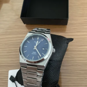 Tre Tissot PRX Quartz herrklocka - Snygg Tissot PRX Quartz herrklocka med en stilren blå urtavla och silverfärgad metallarmband. Klockan har en klassisk design med datumvisning och är perfekt för den som gillar en tidlös look.