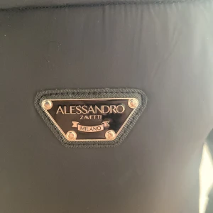 Svart dunjacka från Alessandro Zavetti - Snygg svart dunjacka från Alessandro Zavetti med huva och dragkedja. Jackan har en stilren design med märkets logga på bröstet och huvan. Perfekt för kyliga dagar.