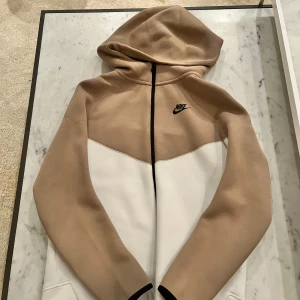 Beige/vit Nike tech hoodie - Säljer min splitternya Nike tech hoodie i färgerna vit/beige. Aldrig använt som sagt så säljer därför av just den anledningen. Inget slitage eller skador 