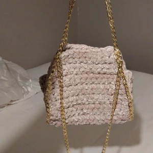 Rosa virkad väska med guldkedja - Säljer en snygg rosa virkad väska med en elegant guldkedja. Väskan har en unik textur och är perfekt för att ge din outfit en stilfull touch. Passar utmärkt som accessoar för olika tillfällen.