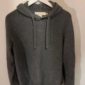Grå stickad hoodie från H&M - Säljer en stilren grå stickad hoodie från H&M (logg) Tröjan har en bekväm huva med dragsko och långa ärmar. Perfekt för kyliga dagar och ger en avslappnad look. Passar bra till jeans eller chinos.