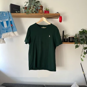 Mörkgrön t-shirt från Ralph Lauren - Säljer en stilren mörkgrön t-shirt från Ralph Lauren med en liten broderad logga på bröstet. T-shirten har en klassisk passform och är tillverkad i mjuk bomull. Perfekt för en avslappnad look.