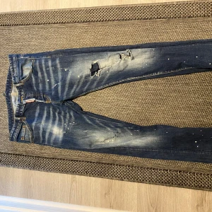 jeans  Dsquared2 - Snygga blå jeans från Dsquared2 med slitna detaljer och en cool tvättad look. De har en normal passform och är dekorerade med små färgstänk. Perfekta för en trendig stil.