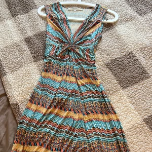 Färgglad ärmlös klänning från RoseBud -  färgglad ärmlös klänning från RoseBud med ett unikt mönster i blått, orange och gult. Klänningen har en v-ringad design med en knutdetalj framtill. Klänningen är lång. Storlek s och i fint skick.