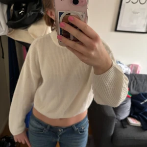 Vit stickad tröja Divided - Säljer en vit stickad tröja från Divided. Tröjan har en lite högre krage, långa ärmar och en croppad look.