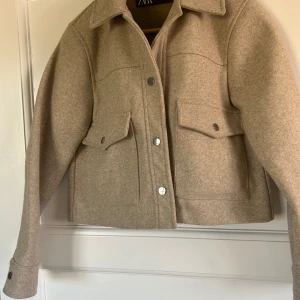 Beige jacka från Zara - Snygg beige jacka från Zara med knappar framtill och två stora fickor med lock. Jackan har en klassisk krage och långa ärmar med knappdetaljer vid ärm sluten💕