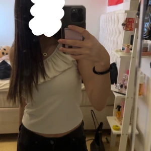 Vit oneshoulder topp med volang - Säljer en stilren vit oneshoulder topp med volangdetalj, köpt här på Plick