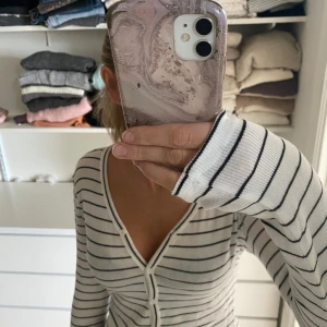 Vit och svart randig kofta - Säljer en snygg vit kofta med svarta ränder. Den har en v-ringad design och knappar framtill. 