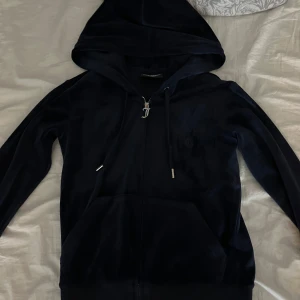 Mörk blå tröja från Juicy Couture - Säljer en snygg mörkblå tröja från Juicy Couture i storlek XS. Den har en dragkedja framtill och en broderad logga på bröstet. Perfekt för en stilren och bekväm look. Använd några gånger, kan ha krympt lite efter att jag har tvättt den men annars är det inga fel på den. Köpte den för 1300 kr säljer för 300 kr. Pris kan diskuteras!!