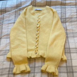 Gul kofta från Zara med volanger  - Säljer en söt gul kofta från Zara med volangdetaljer vid ärmslut och nederkant. Koftan har knappar framtill och är perfekt för en mysig dag. Den är långärmad och gjord i ett mjukt material. Koftan är inte tillgänglig längre på Zara men finns i andra färger! Använd en gång och tvättad en gång! Den är i storlek s och den passar mig som är ca 164cm 🩷