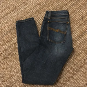 Mörkblå jeans från Nudie Jeans - Snygga mörkblå jeans från Nudie Jeans med klassisk femficksdesign och kontrastsömmar. Jeansen har en slim passform och är tillverkade i högkvalitativt denim. Perfekta för en stilren look. Storlek w26L30 Jeansen är bra i ett bra skick och är bara använda i några månader 