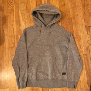 Grå hoodie från Jack & Jones - Säljer en klassisk grå hoodie från Jack & Jones. Den har en stor ficka framtill och justerbar huva med dragsko. Perfekt för en avslappnad stil. 🩶