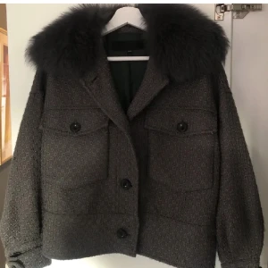 Svart Meotine Kappa/Jacka - Snygg svart kappa med pälsdetalj på kragen. Jackan har ett diskret mönster och stora knappar framtill. Saknas dock en knapp längst ner på höger armen men ej så märkbart då jag dragit ner ärmarna. Nypris 3000
