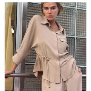Beige skjorta med knytning - Snygg beige skjorta med knytning i midjan och en bröstficka. Skjortan har långa ärmar som kan rullas upp och fästas med knapp. Perfekt för en stilren look. Du kan styla denna tröja på många sätt!! Helt ny i storlek M💕💕
