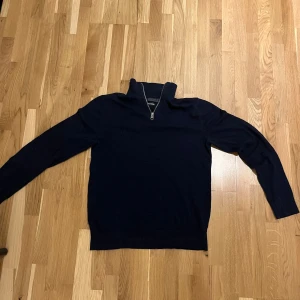 Mörkblå tröja med dragkedja - Säljer en stilren mörkblå tröja från Jack and Jones med dragkedja vid halsen. Tröjan har långa ärmar och en klassisk passform. Perfekt för kyligare dagar. Strorlek Xs men passar även S