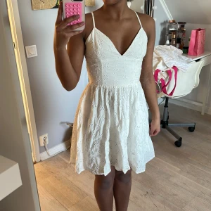 Vit spetsklänning - Söt vit klänning med smala axelband och v-ringning. Klänningen har ett vackert spetsmönster och är perfekt för sommarens alla tillfällen. Den är kort och luftig, vilket gör den idealisk för varma dagar. 