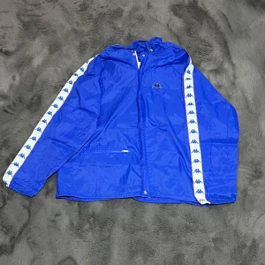 Rare Vintage Kappa Windbreaker 1980- Mycket bra skick! - Säljer en unik vintage Kappa windbreaker i blå färg, med klassiska Kappa-loggor på ärmarna. Detta är en made in Italy-modell och en officiell sponsorjacka för US Track & Field Team, vilket gör den både sällsynt och samlarvärd!  ✔ Märke: Kappa ✔ Färg: Djupblå med Kappa-loggor på ärmarna ✔ Storlek: 48 (passar ungefär M/L – se mått!) ✔ Material: Lättviktigt och vindtätt tyg, perfekt för vår & höst ✔ Passform: Regular fit – sportig och avslappnad stil ✔ Skick: A (Utmärkt skick för sin ålder,)