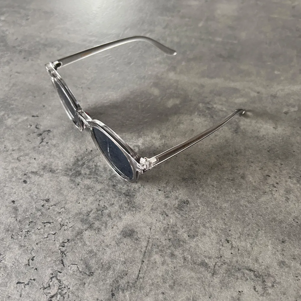 Snygga solglasögon med transparent båge och runda, mörka linser. Perfekta för en stilren look. Passar både till stranden och stadspromenaden.. Asusteet.