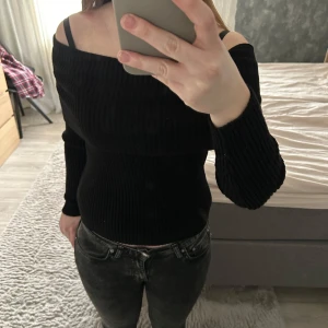 Svart offshoulder tröja - Säljer en stilren svart offshoulder tröja med ribbad design. Tröjan har långa ärmar och en tight passform. Perfekt för en trendig look.