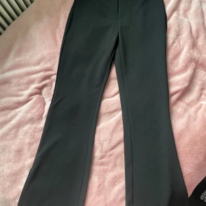 Svarta kostymbyxor med dragkedja - Snygga svarta kostymbyxor med en klassisk bootcut-stil. Byxorna har en praktisk dragkedja och en knapp i midjan för enkel stängning.  