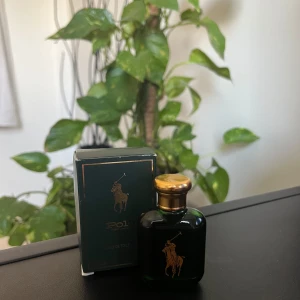 Polo Eau de Toilette 15 ml - Säljer en elegant Polo Eau de Toilette från Ralph Lauren i en stilren grön flaska med gulddetaljer. Flaskan rymmer 15 ml och kommer i en matchande grön kartong med den ikoniska polospelaren i guld. Perfekt för den som vill ha en klassisk och tidlös doft.