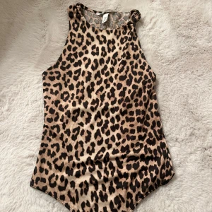 Leopardmönstrad ärmlös bodysuit - Säljer en snygg ärmlös bodysuit med leopardmönster. Perfekt för dig som vill sticka ut med ett djurmönstrat plagg. Hög halsringning och mjukt material som sitter tight mot kroppen.