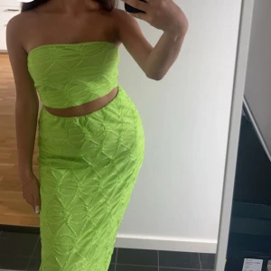 Limegrön tvådelad klänning - Säljer en limegrön tvådelad klänning med tubtopp och lång kjol. Klänningen har ett snyggt mönster och är perfekt för dig som vill sticka ut. Kjolen är figurnära och toppen är axelbandslös. Strl XS i kjolen och strl S i topp