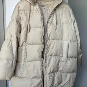 Beige pufferjacka med huva från Zara - Säljer en beige pufferjacka från Zara med huva och dragkedja. Jackan är oversized och har långa ärmar samt två stora fickor framtill. Perfekt för kyliga dagar och enkel att matcha med olika outfits.