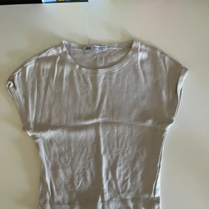 Beige och vit topp från Zara - Tre  toppar från Zara i storlek S. En beige och en vit, och en till vit fast i lite tjockare material med en tjockare hals,alla med rund halsringning och korta ärmar. Perfekta att matcha med jeans eller kjol för en enkel och snygg look. Skrynkliga då jag tvättat alla precis. Strykning sker innan leverans