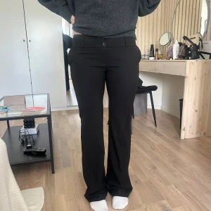 Svarta kostymbyxor med bootcut - Säljer ett par svarta lågmidjade kostymbyxor med bootcut passform. Byxorna har klassisk design med knapp och dragkedja framtill samt fickor bak. Det står på lappen att det är storlek 38 men skulle säga att den är 36/34.