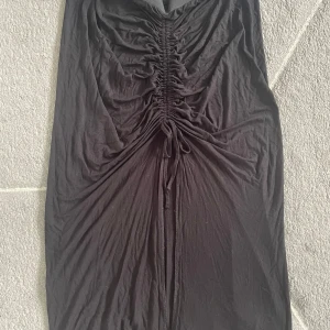 Svart långkjol med rynk och knyt från Lindex - Säljer en svart långkjol från Lindex med snygg rynkdetalj och knyt framtill. Kjolen har elastisk midja och är tillverkad i ett mjukt, stretchigt material. Perfekt för dig som gillar en stilren och trendig look.