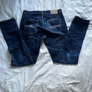 Mörkblå nudie jeans - Säljer ett par mörkblå nudie jeans i bra skick. De har en slim passform och är perfekta för både vardag och fest. Klassisk design med fem fickor och knappgylf. Passar till det mesta i garderoben!