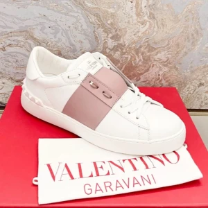 Valentino Garavani Open sneakers med rosa band - Snygga vita sneakers från Valentino Garavani med ett brett ljusrosa band över vristen och nitar på hälen. Skorna har rund tå, platt sula och klassisk snörning. Perfekta för dig som vill ha en stilren men ändå unik look.