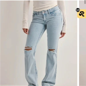 Ljusblå lågmidjade bootcut jeans från Nelly - Säljer ett par ljusblå bootcut jeans från Nelly med slitna detaljer vid knäna och rosa broderade bakfickor.💕💕💕storlek 36!