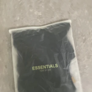 Essentials t shirt  - Säljer en svart t-shirt från Fear of God Essentials med tryckt logga på bröstet. Klassisk passform och rund halsringning. Perfekt för dig som gillar streetwear och vill ha en stilren look.