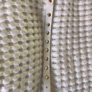 Vitt armband  med guldfärgade nitar - Säljer ett smalt vitt armband  med guldfärgade runda och fyrkantiga nitar längs hela bandet. Perfekt accessoar för att ge outfiten lite edge. Bältet har flera hål för justerbar passform.