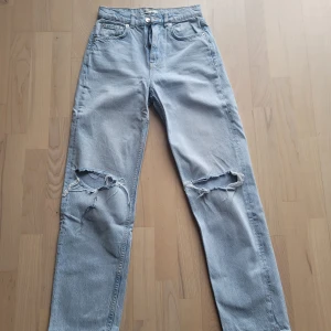 Ljusblå jeans med slitningar från gina tricot - Säljer ett par ljusblå jeans från Gina Tricotl med raka ben och stora slitningar över båda knäna. Jeansen har klassisk femficksdesign och hög midja. Perfekta för en avslappnad och trendig look. Slitningar vid knä fanns där vid inköp. Köpare står för frakten 