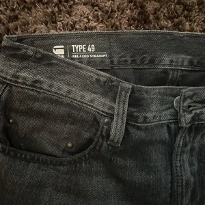 Svarta jeansbyxor från G-Star RAW Type 49 - Säljer ett par svarta G-Star RAW Type 49 jeans med relaxed straight fit. Klassisk femficksmodell med läderpatch bak och broderad logga vid bakfickan. Snygg tvättad finish och raka ben.