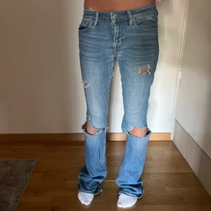 Ljusblå slitna jeans från Crocker - Säljer ett par ljusblå bootcut jeans från Crocker med slitningar och hål vid knäna. Jeansen har normal passform. Perfekta för en avslappnad och trendig look.