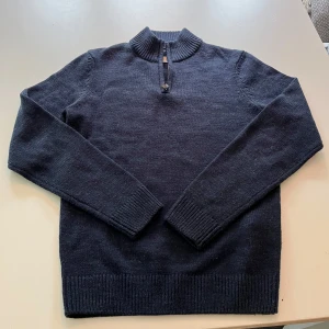 Mörkblå stickad tröja med dragkedja från Pier One - Mörkblå stickad tröja från Pier One med halv dragkedja vid halsen och ribbade muddar. Perfekt för kyliga dagar och enkel att matcha med jeans eller chinos.