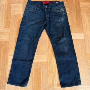Mörkblå Replay jeansbyxor W 31 L 34 - Säljer ett par mörkblå jeans från Replay med raka ben och klassisk femficksdesign. Byxorna har röda detaljer vid fickorna och Replay-logga på myntfickan. Perfekta för dig som gillar en tidlös jeansstil.