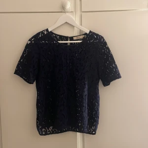 Mörkblå spetsblus från 365 - Säljer en mörkblå blus i spets från 365. Blusen har korta ärmar, rund halsringning och knappar längs ryggen. Perfekt för dig som gillar detaljer och ett elegant spetsmönster.