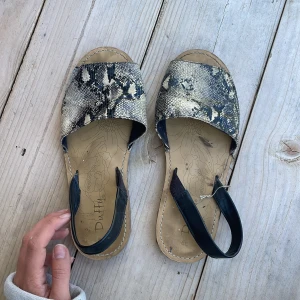 Ormmönstrade sandaler - Säljer ett par snygga sandaler från Duffy med svart och beige ormmönster. Skorna har öppen tå, platt sula och en svart rem runt hälen. 