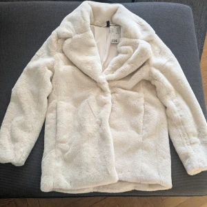 Vit pälsjacka med krage - Säljer en fluffig vit pälsjacka från H&M med bred krage och lång ärm. Jackan har en lyxig känsla och är perfekt för att hålla värmen under kyliga dagar. Enkel att matcha med olika outfits.
